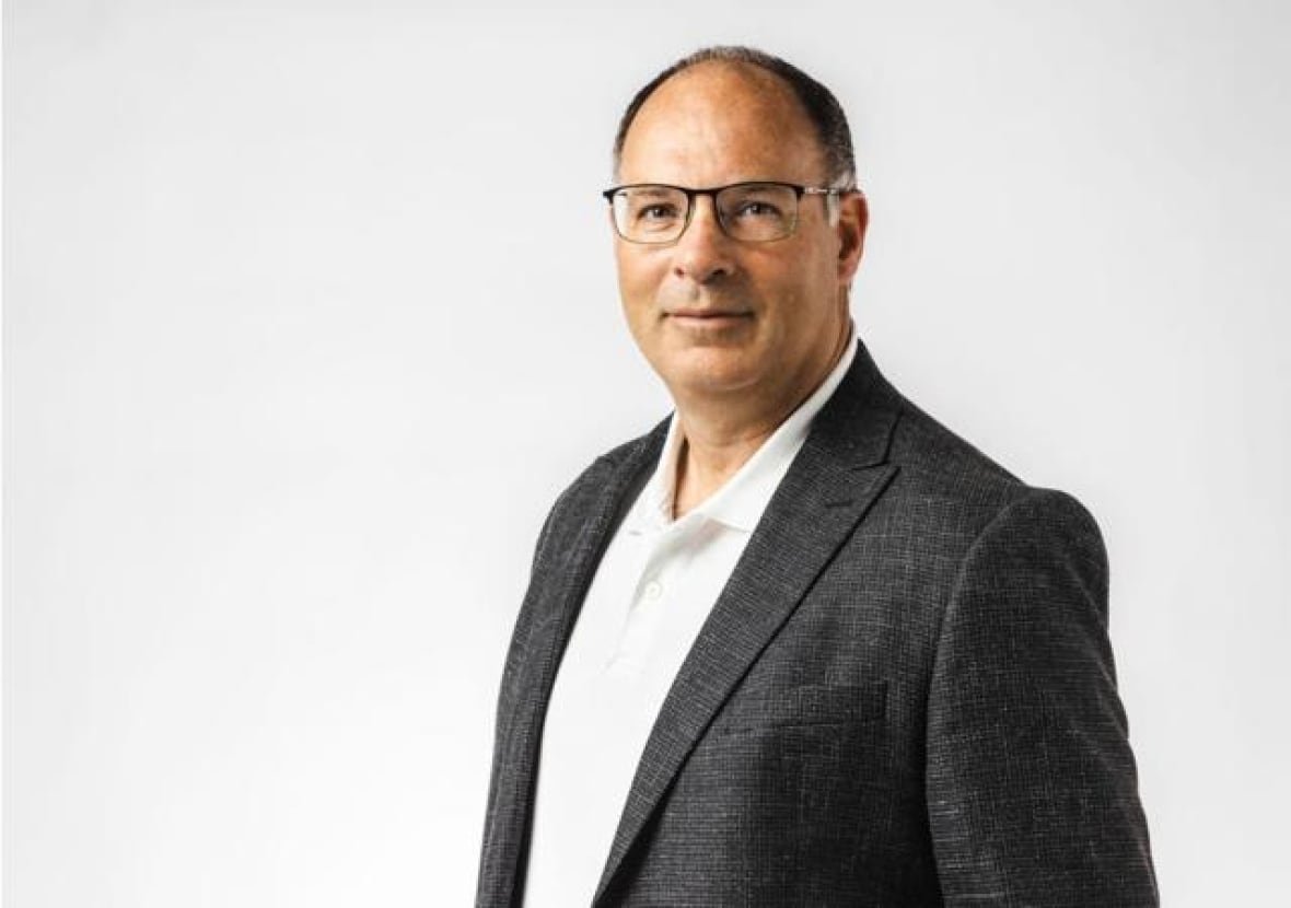 A man wearing a black suit and glasses is smiling at the camera. 