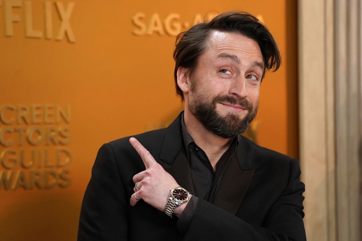 A person smiles while pointing a finger above their shoulder.