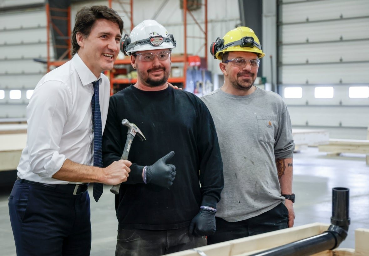 A man holding a hammer smiles alongside two people wearing hard hats.