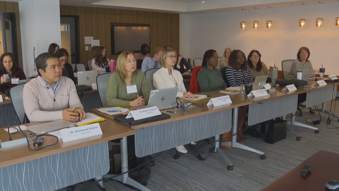 A group of people sit at long tables with name placards at each space. 