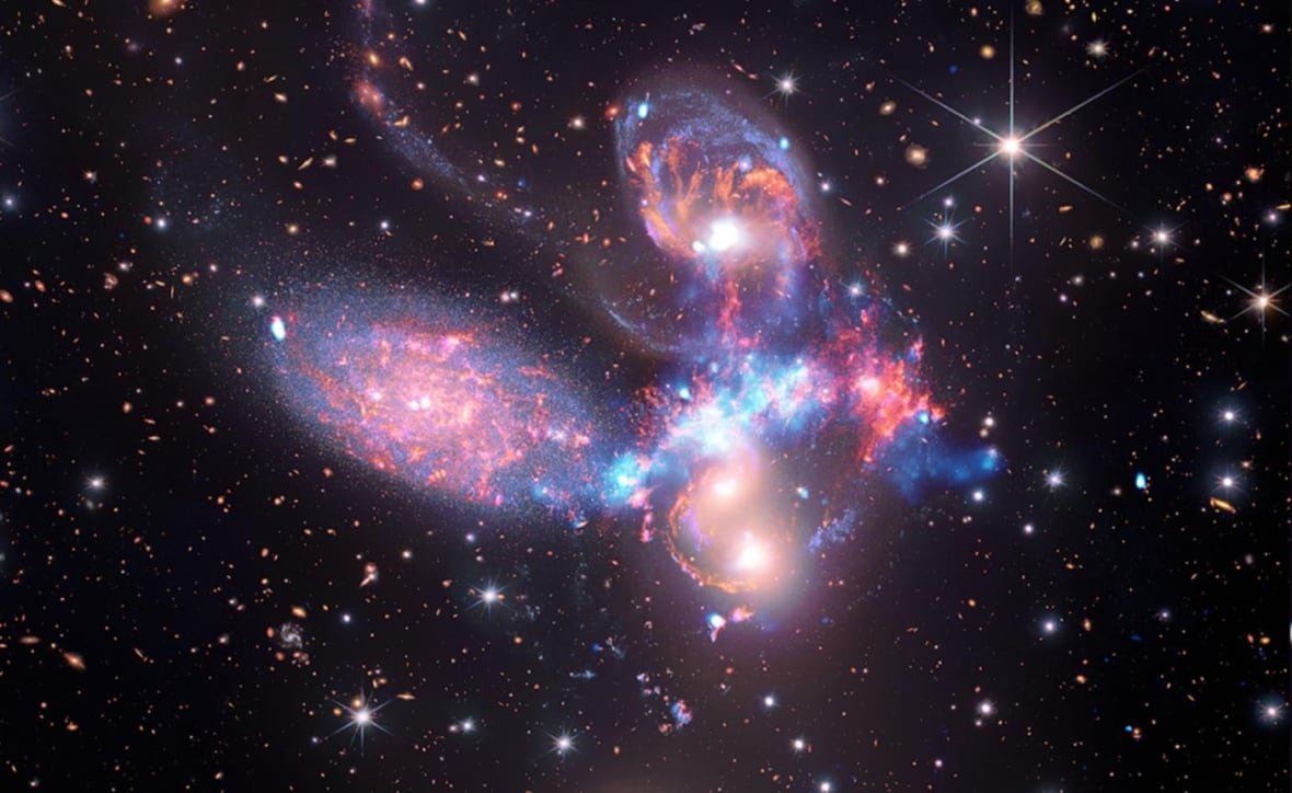 Four bright objects in space surrounded by galaxy light are clustered in space. 