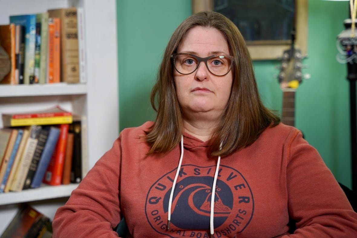 Woman wearing an orange hoodie poses in front of a bookshelf