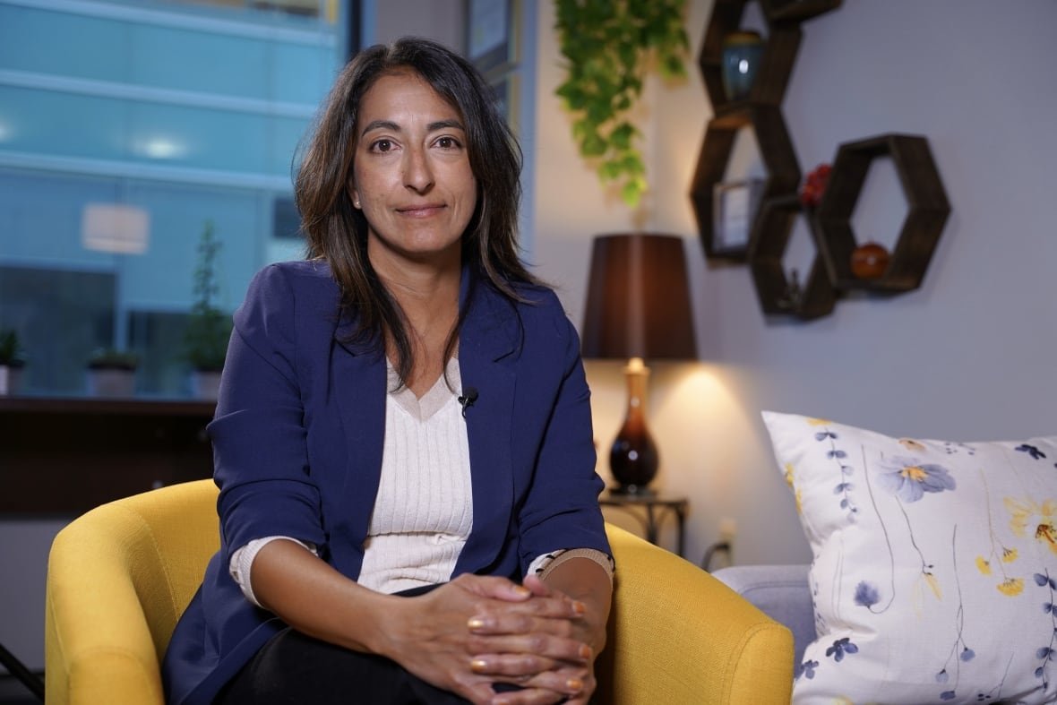woman sitting in a yellow chair wearing a blue blazer looks into the camera