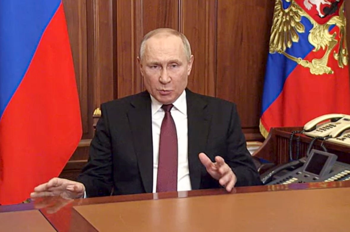 A man sits at a desk with a Russian flag visible.