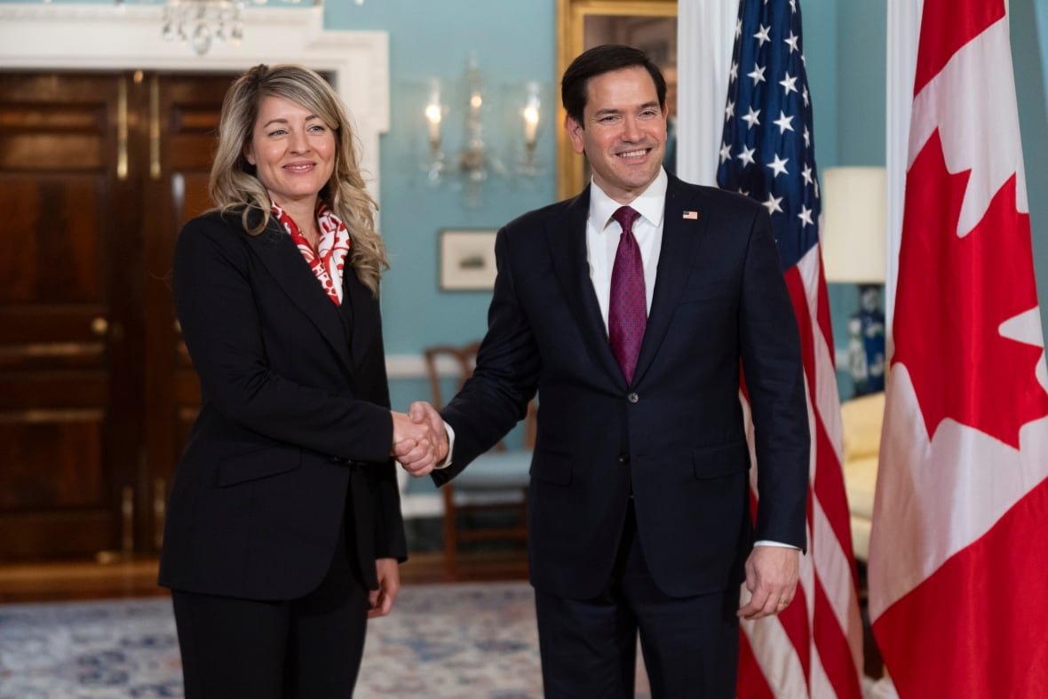 A man and a woman shake hands beside Canadian and U.S. flags.