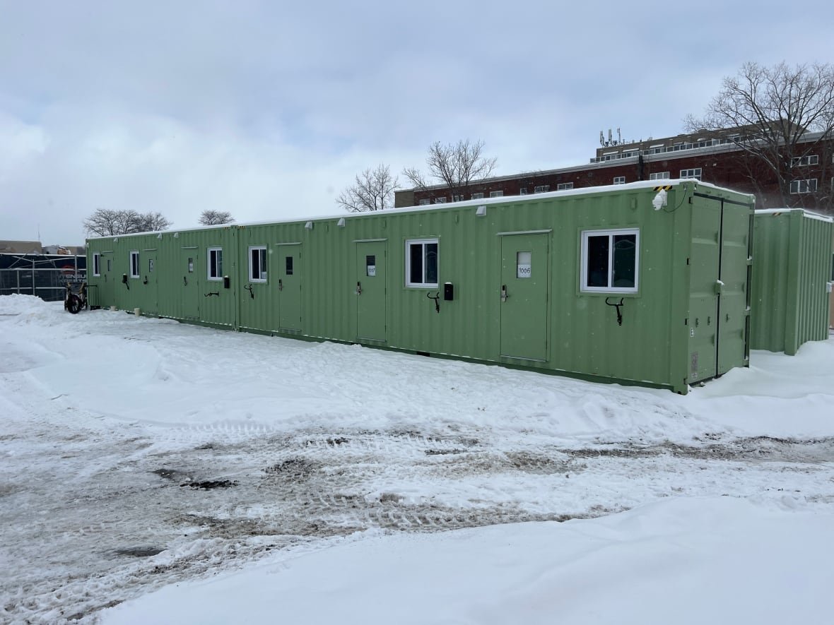 Shipping containers are seen outside during the winter. They have been turned into small homes, with a window and door on the front, and a place to lock a bike.