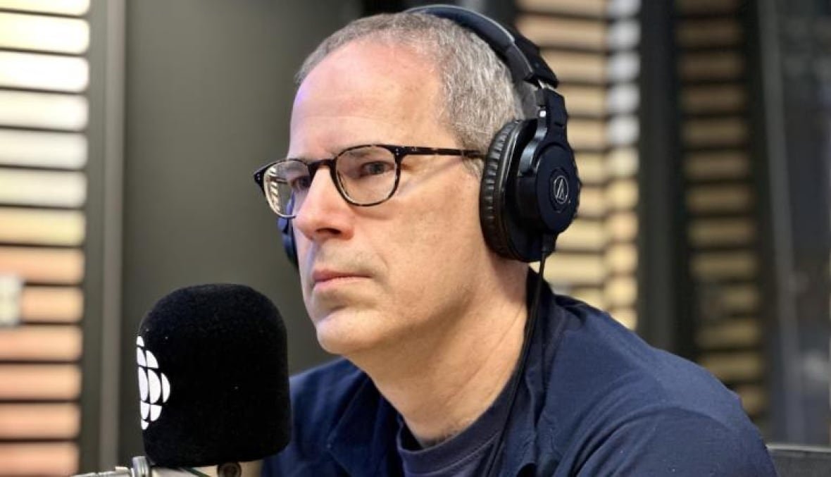 A man wears headphones and sits in front of a microphone in a radio studio.