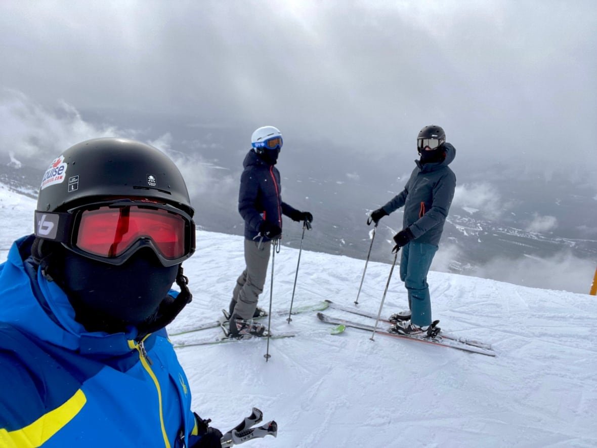 Three people in snowsuits and ski goggles standing on a snowy ski hill. 