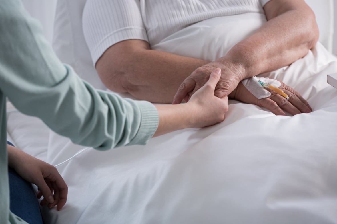 The photo shows a woman holding onto the hand of someone who is lying in a hospital bed. 