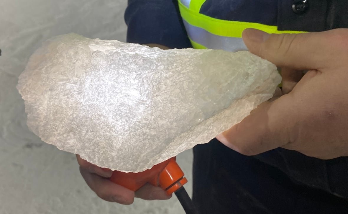 Miner holds a rock of salt about the size of a shoe while shining a light through it. 