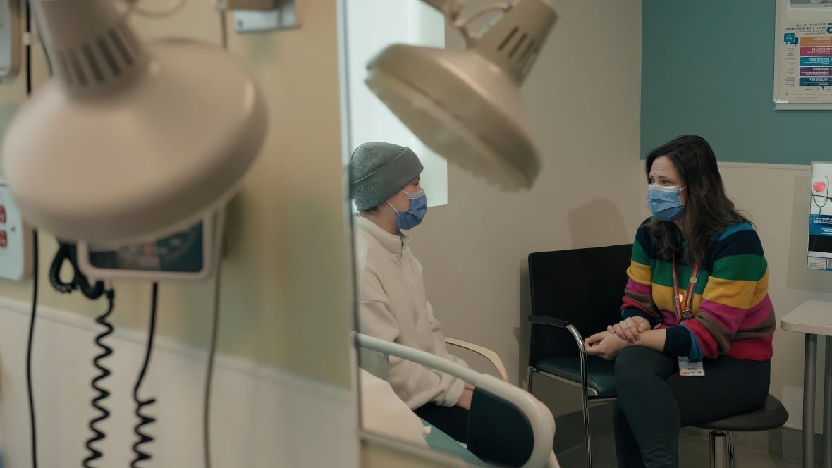 A nurse and a young cancer patient are talk to each other in a clinical setting.