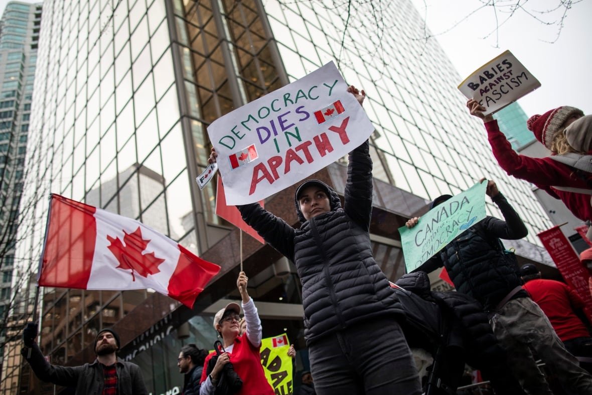 Protestors hold signs and Canadian flags