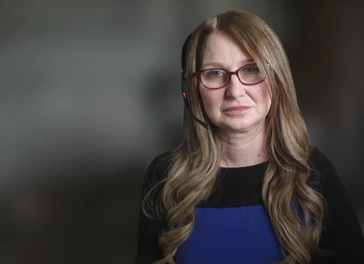 A woman in a blue and black shirt wears a headset for a video call.
