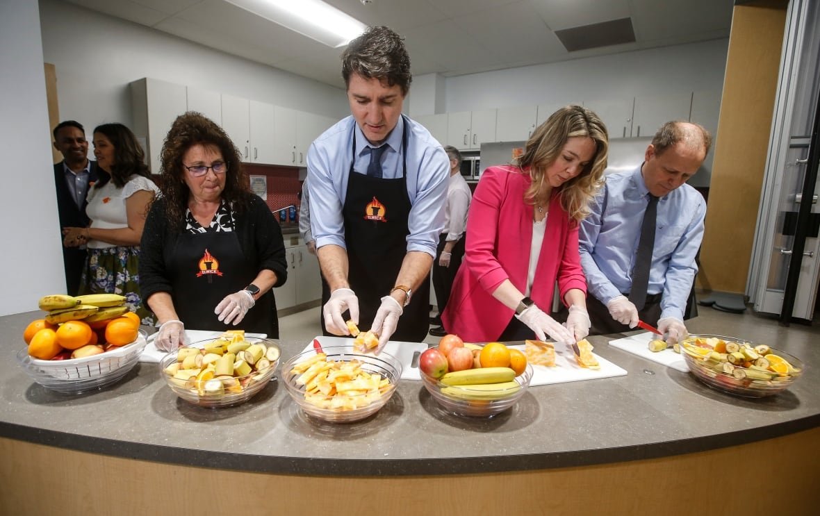 Educational assistant Kim Jemielity (left) cuts up fruit for students while wearing disposible gloves at a counter alongside Prime Minister Justin Trudeau, Social Development Minister Jenna Sudds and Liberal MP Kevin Lamoureux at Elwick Community School in Winnipeg on May 17.