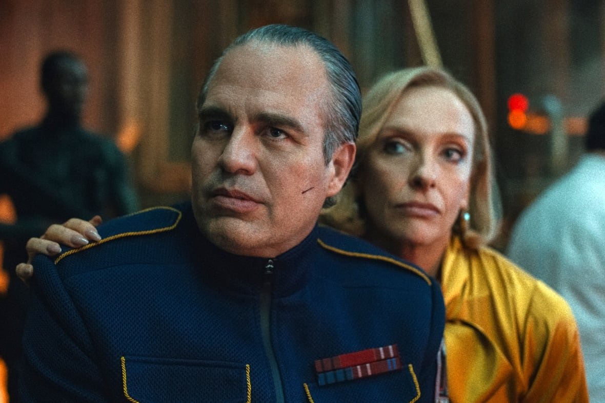 A man wearing a military suit is embraced from behind by a woman.