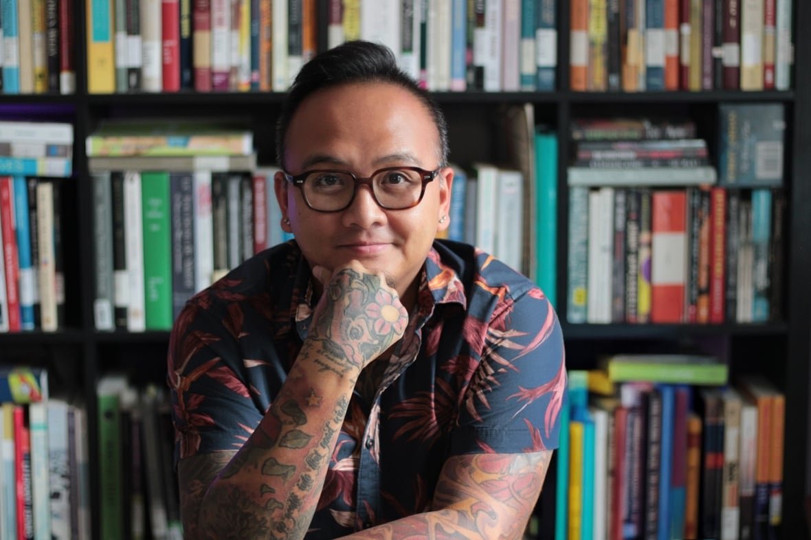 A man smiles at the camera with bookshelves behind him.