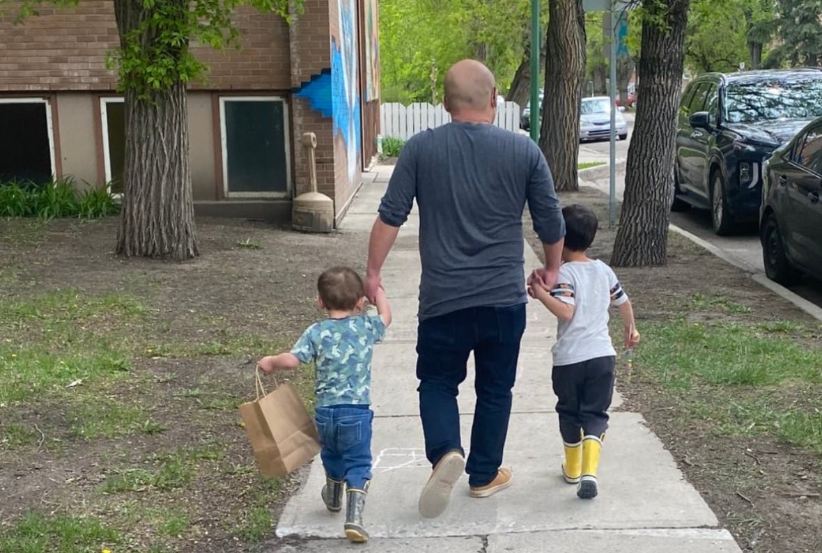A man walks down the sidewalk, holding the hands of two children. 