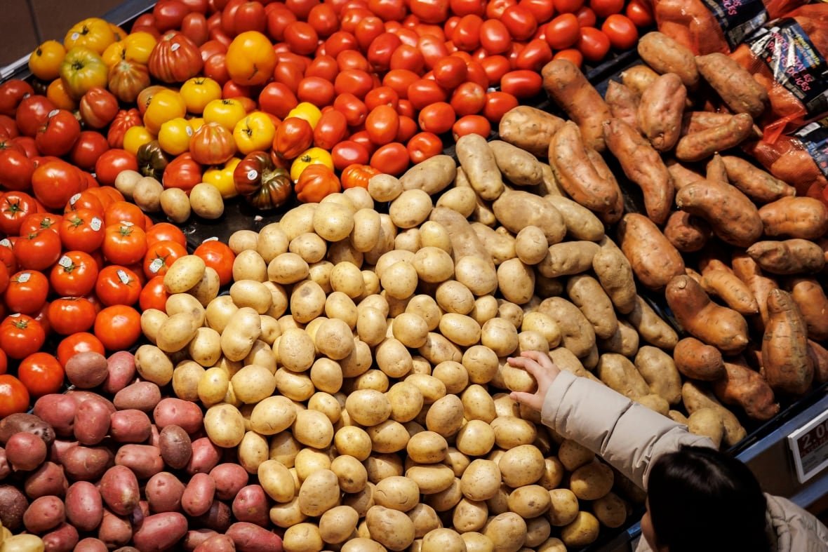 A person reaches for a potato at a grocery store.
