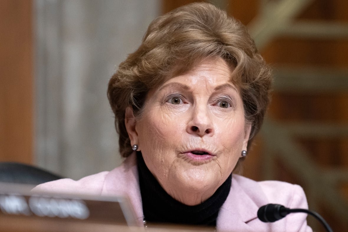A woman in a pink blazer speaks into a microphone