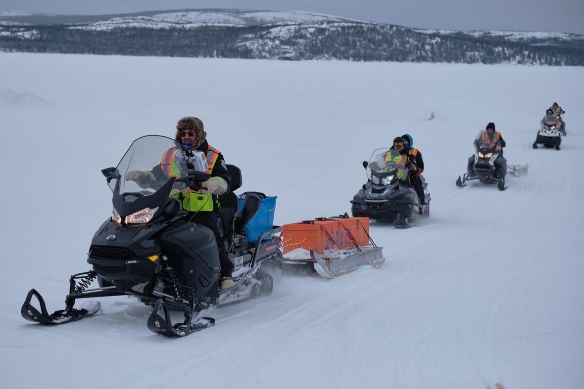 People riding snowmobiles on the snow pulling technology behind them. 