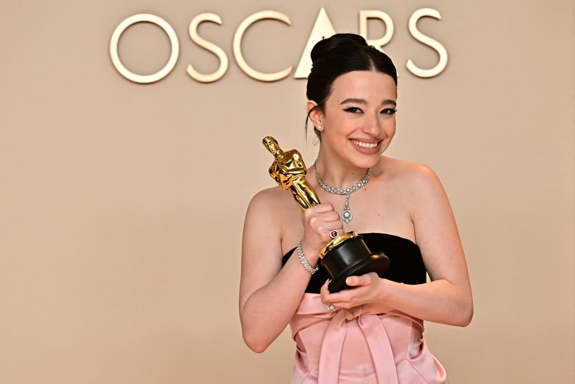 A smiling woman poses with a trophy in front of the word Oscars.