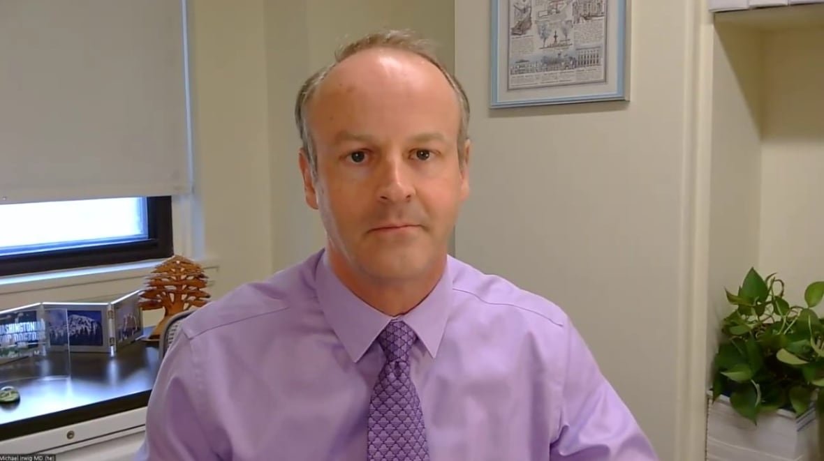 A person sits in an office with a plant and photographs in the background.