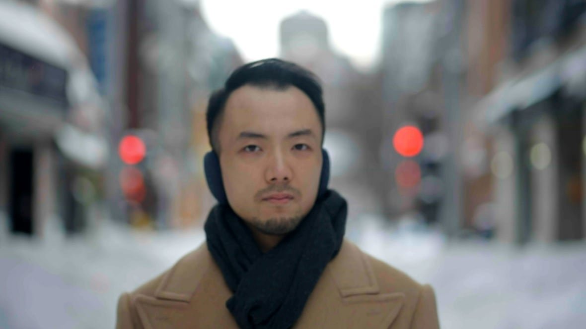 A person stands outside with a city streetscape behind them.