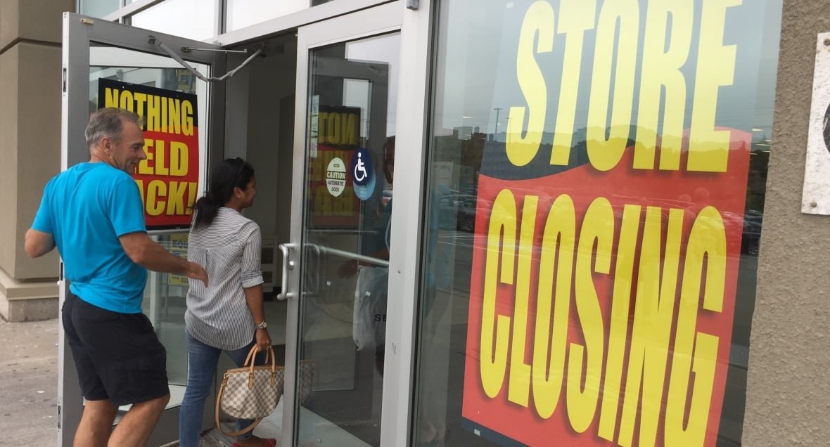 Two people walking into a Sears store holding liquidation sales. 