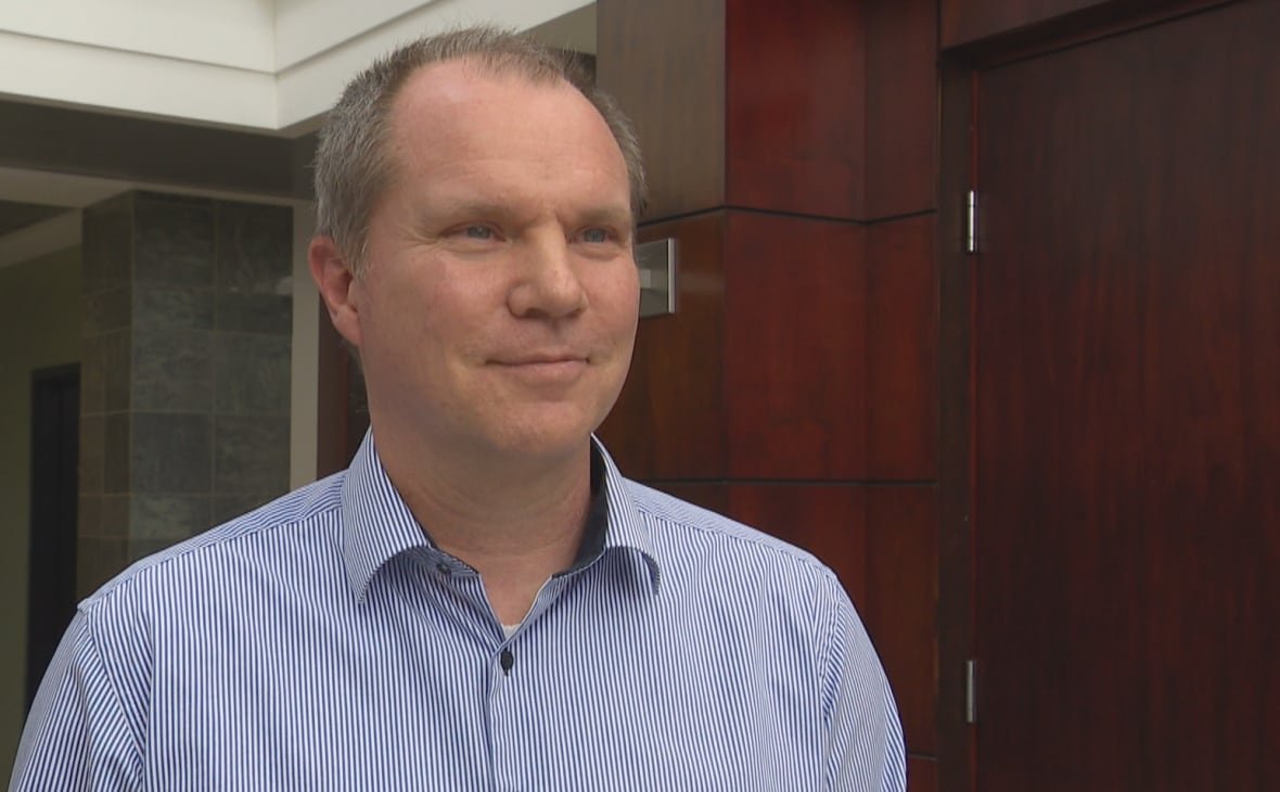 A man in a striped button-up shirt stands inside a building.