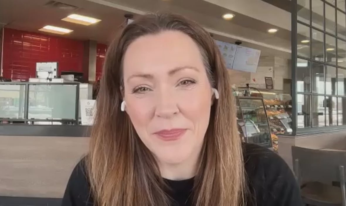 A woman with long brown hair sits at a table in a Tim Hortons restaurant, with the counter and display visible in the background.