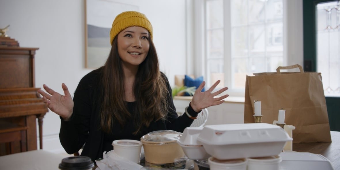 Science journalist Ziya Tong sits at a table with various plastic takeout containers on it.