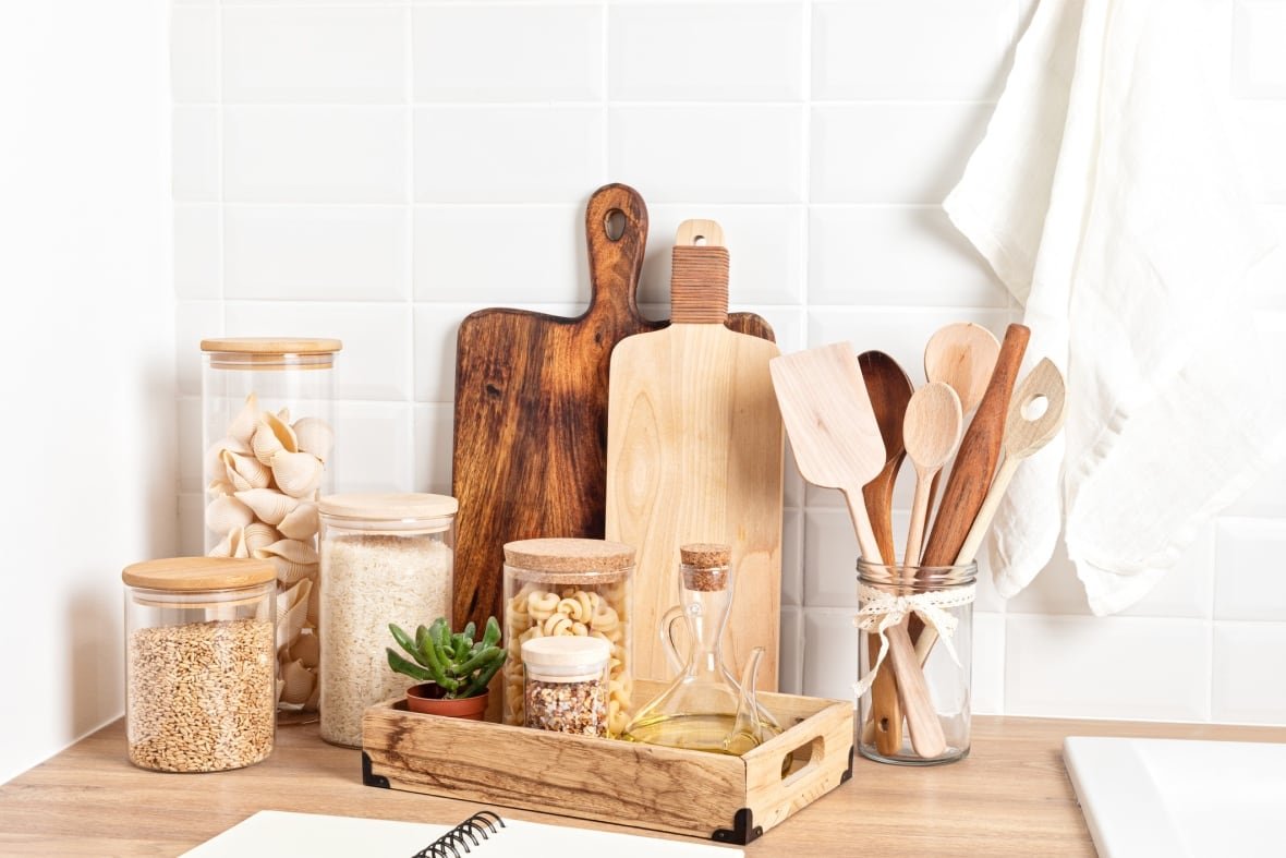 A photograph of a variety of wood, bamboo, and glass kitchen equipment such as cutting boards, utensils, and storage containers together on a kitchen counter.