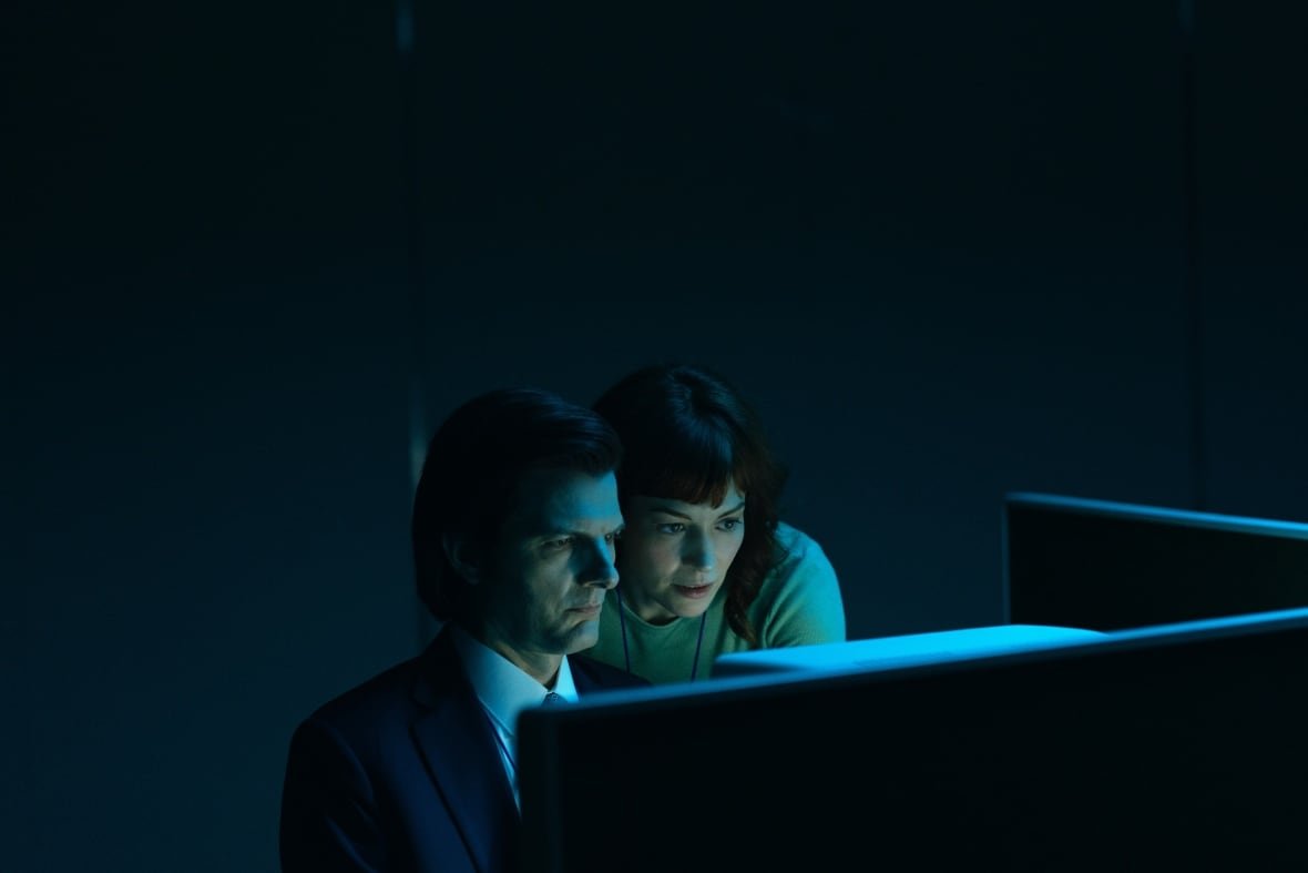 Two people lean over a computer in a dark room