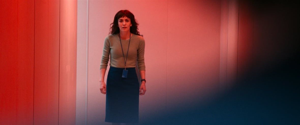 A woman stands in a hallways with red lights flashing