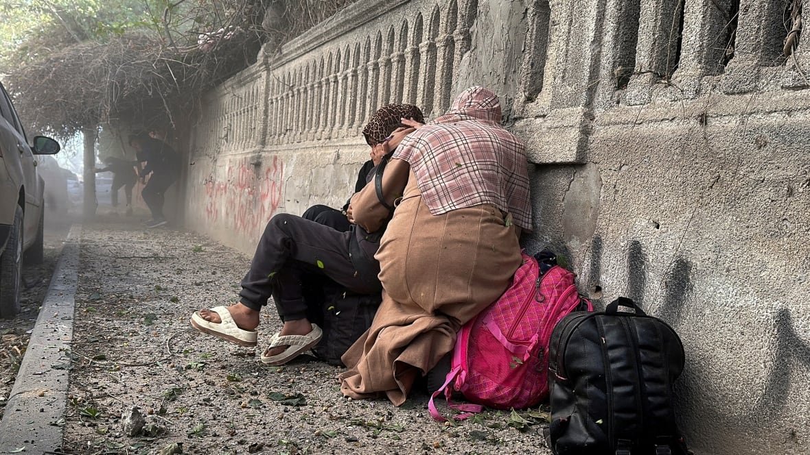 People cower against a wall as debris and dust fill the air.