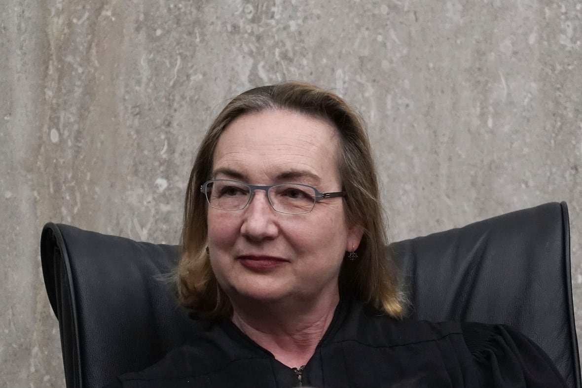 A bespectacled woman wearing glasses and a judicial robe is shown in closeup.