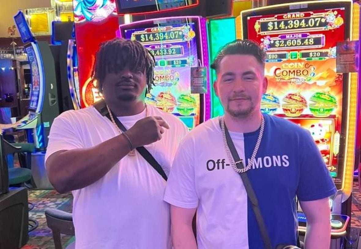Two men photographed standing in front of slot machines