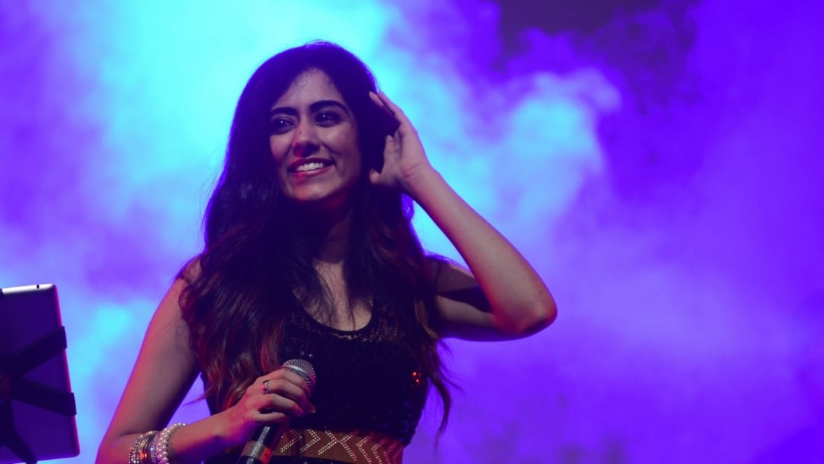A smiling woman holding a microphone stands in front of a wall of smoke. 