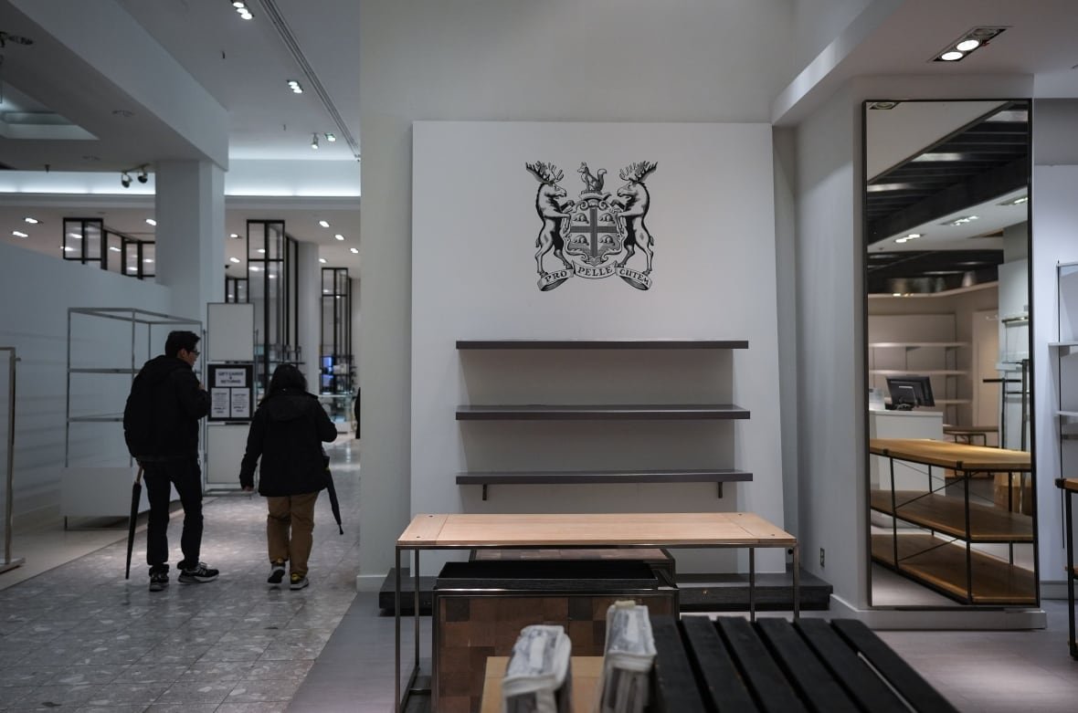 Shoppers walk past empty shelves in a store.