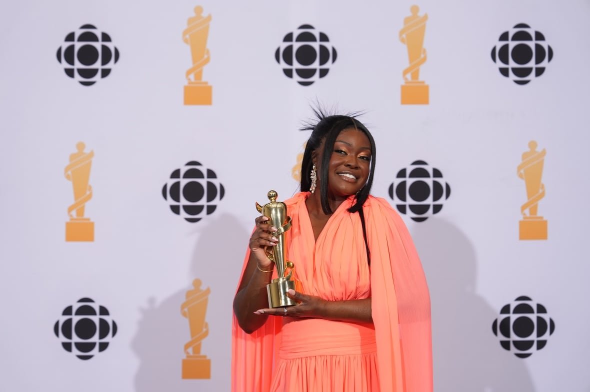 A woman dressed in an orange dress poses for a photo showing off a trophy she just won.