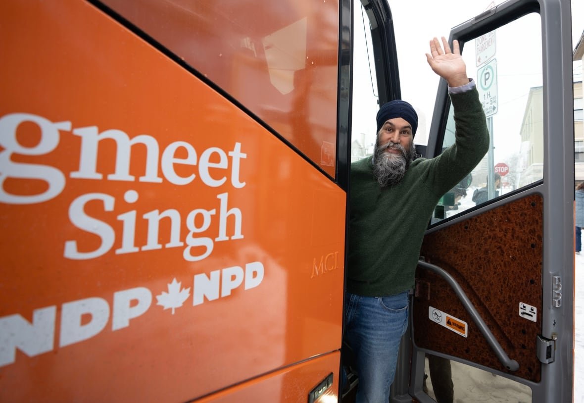 A man standing half inside a bus waves to people in front of him.