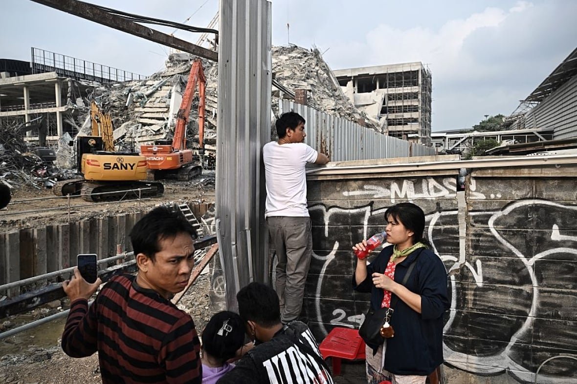 Five people wait at the site of a tower collapse following an earthquake 