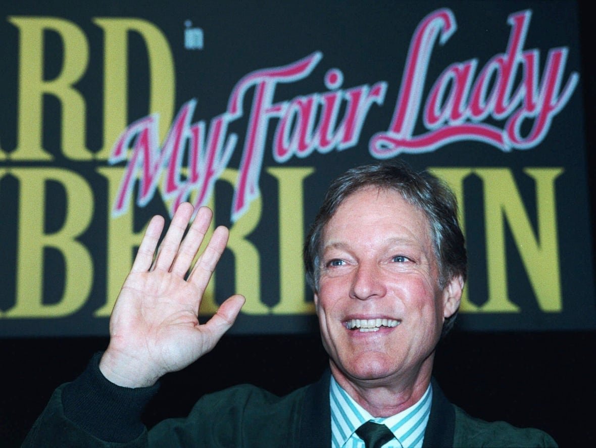 A man waves while posing for a photo.