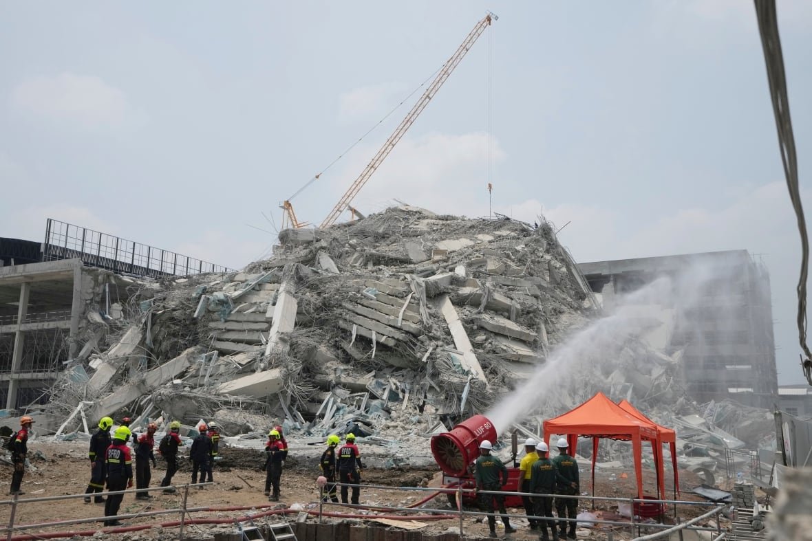 Workers spray water on the rubble of a collapsed building.