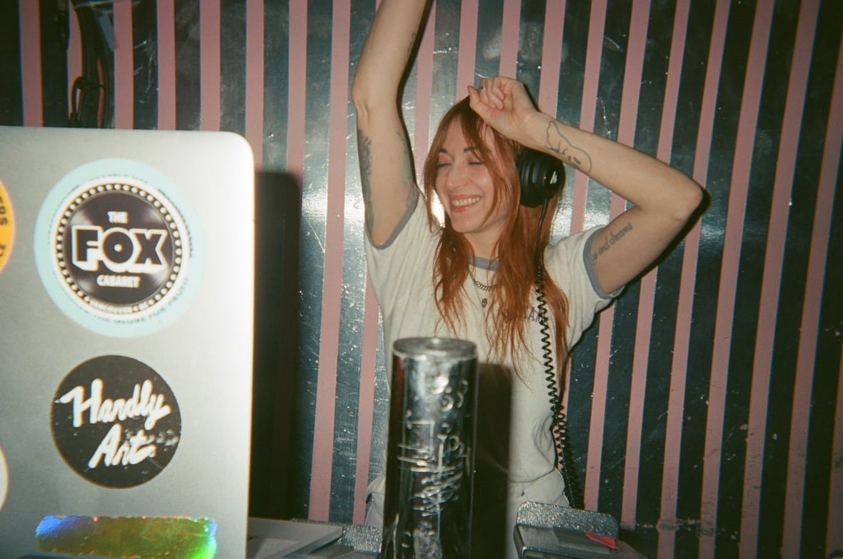 A woman wearing headphones stands in front of a computer dancing