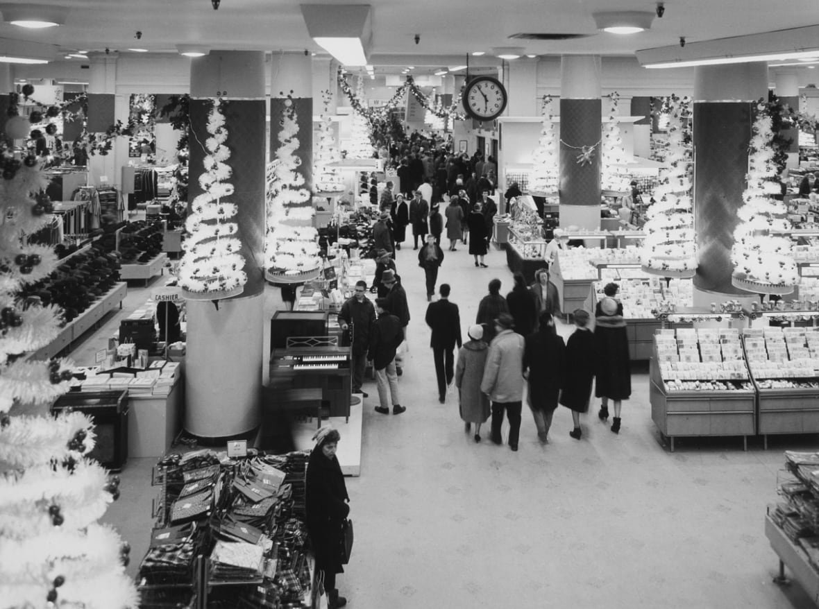 A black and white photo of shoppers in a department store, decorated for Christmas.