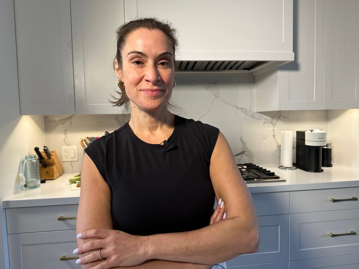 A woman stands with her arms crossed inside of a kitchen.