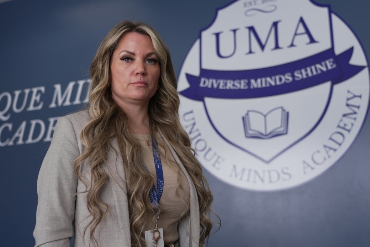 A woman stands in front of a sign that says, Unique Minds Academy.