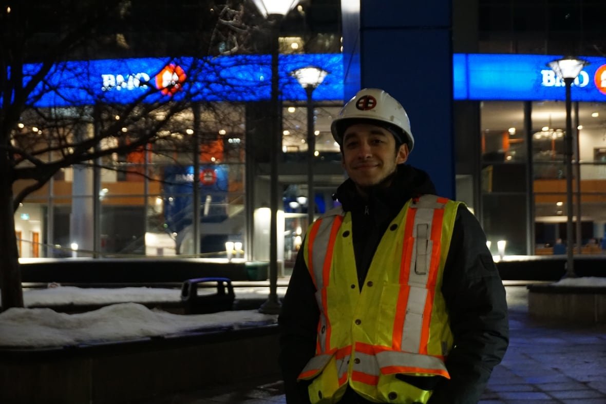 A man wearing a hard hat and safety vest smiles at the camera.