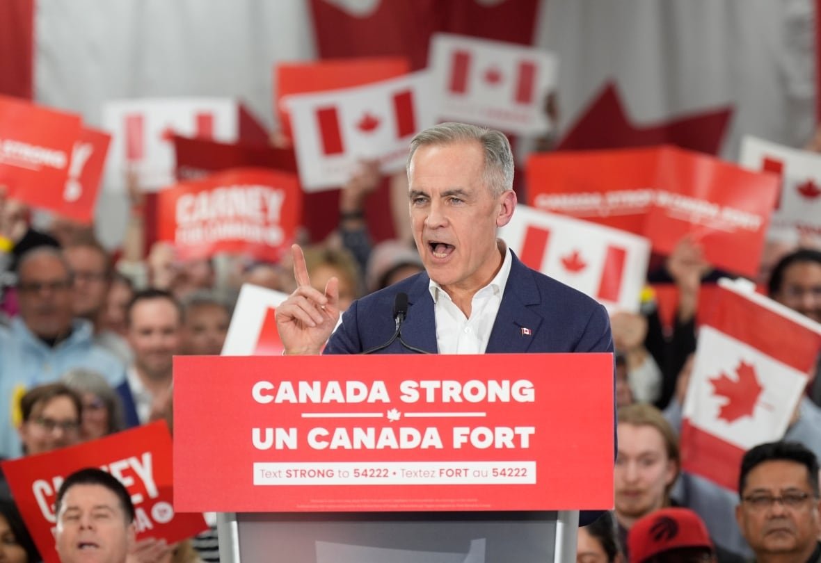 A middle aged white man addresses a crowd holding Liberal party and "Carney" signs. 